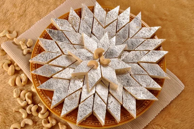 A slice of kaju katli, silver‑leafed and dusted, on a Mishran plate.